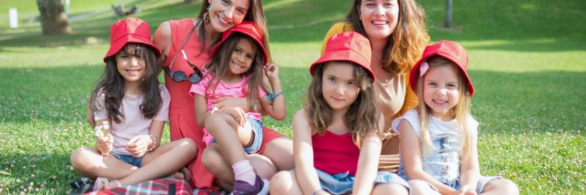 Friends enjoying a sunny day picnic on grass with bucket hats and smiles in a Portuguese park.