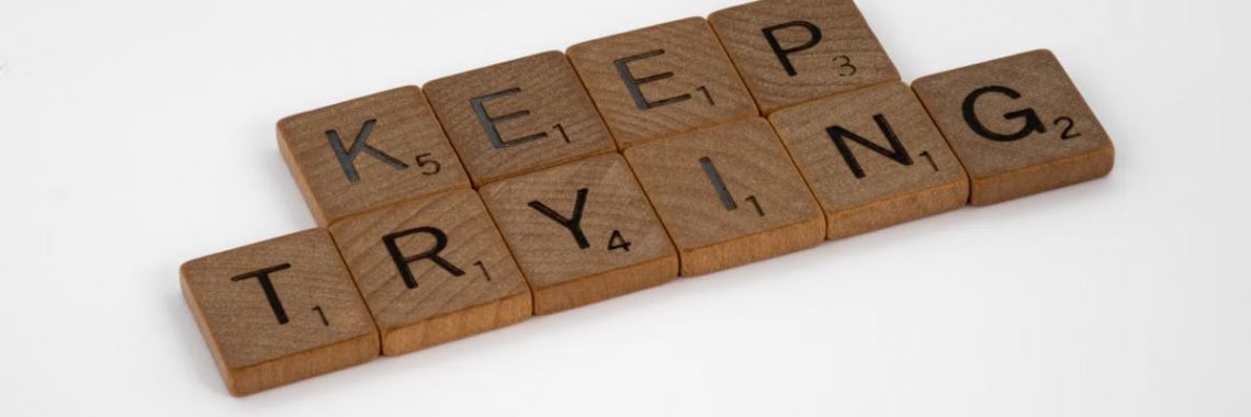 Scrabble tiles form an inspiring message 'Keep Trying' on a white background. Motivational and clean aesthetic.